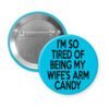 Blue pinback button with text 'I'm so tired of being my wife's arm candy' printed in black.