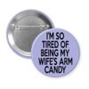Purple pinback button with text 'I'm so tired of being my wife's arm candy' printed in black.