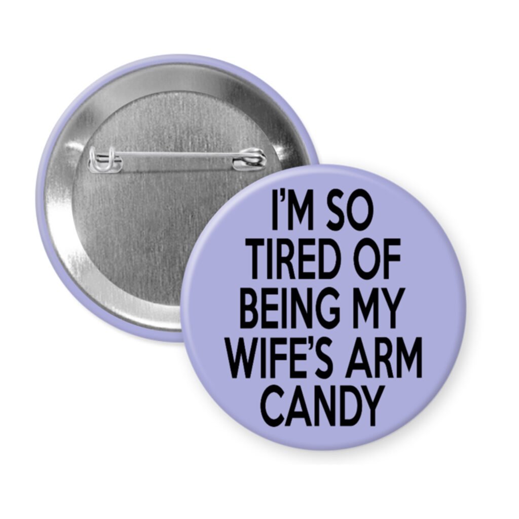 Purple pinback button with text 'I'm so tired of being my wife's arm candy' printed in black.
