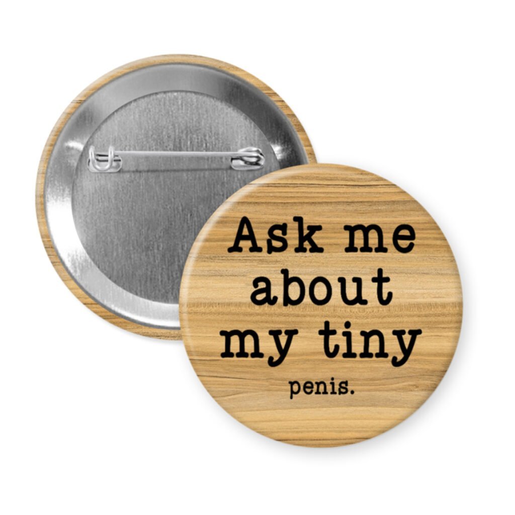 Wood grain print pinback button with text 'Ask me about my tiny penis' printed in black.