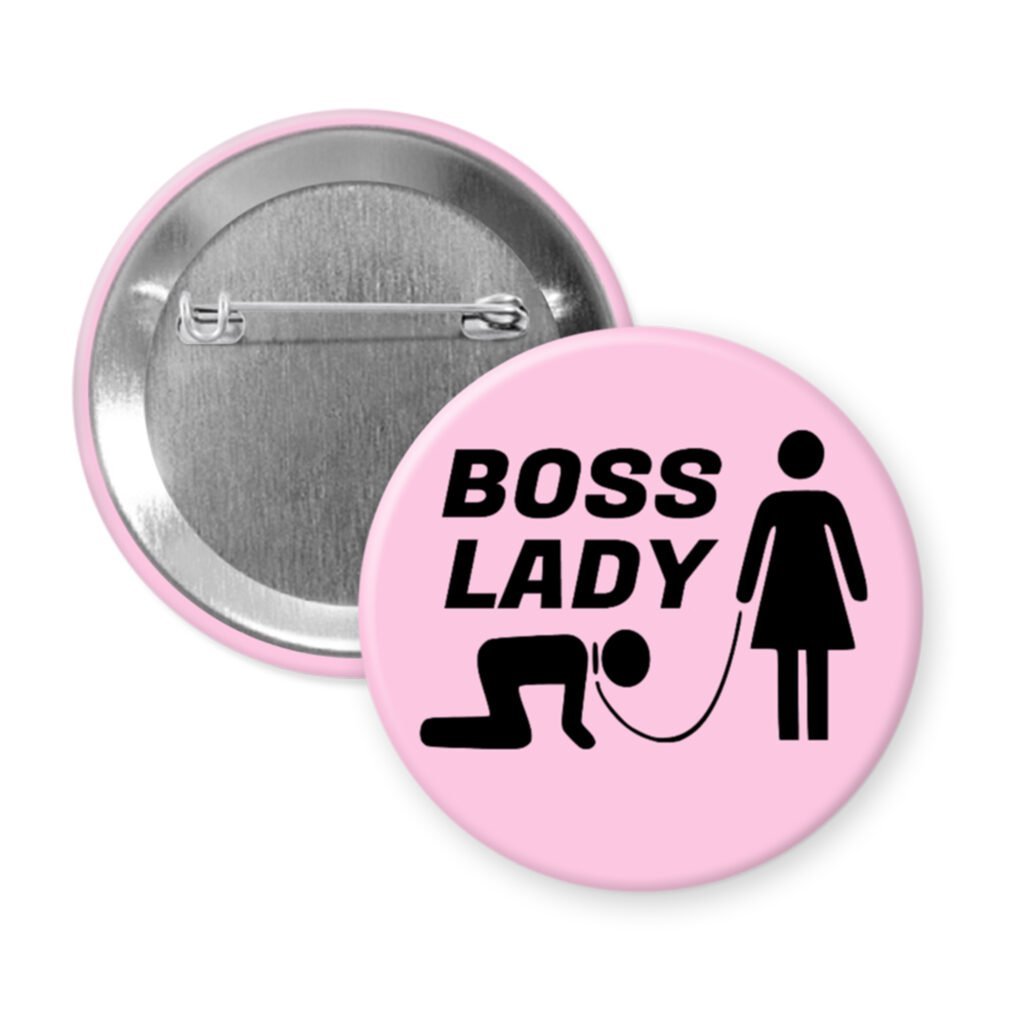 Light pink pinback buttonwith a graphic of a collared and leashed man on hands and knees, a woman figure holding the leash with the text 'BOSS LADY' printed in black.