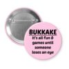 Pink pinback button with the text 'Bukkake- It's all fun & games until someone loses an eye' printed in black.