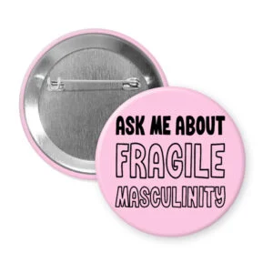 Pink pinback button with the text 'Ask me about fragile masculinity' printed in black.