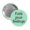 Mint green pinback button with the text 'Fuck your feelings' printed in black.