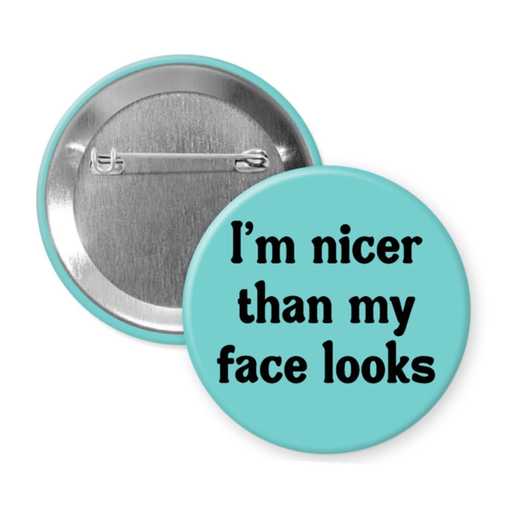 Blue pinback button with the text 'I'm nicer than my face looks' printed in black.