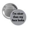 Grey pinback button with the text 'I'm nicer than my face looks' printed in black.