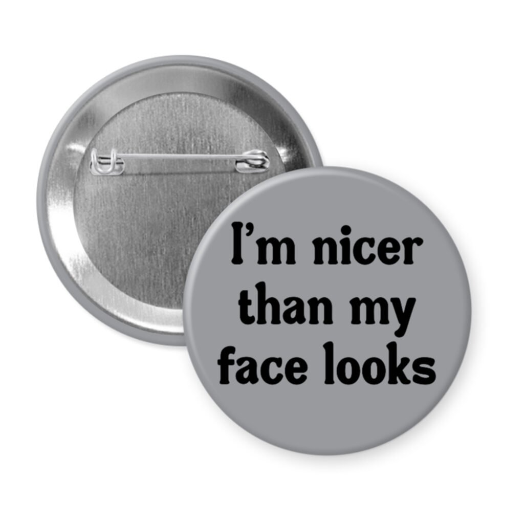 Grey pinback button with the text 'I'm nicer than my face looks' printed in black.