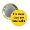 Yellow pinback button with the text 'I'm nicer than my face looks' printed in black.