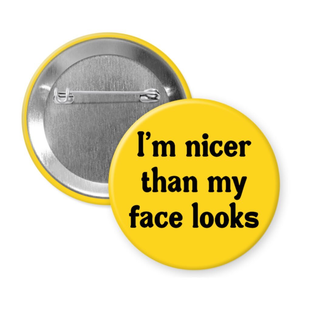Yellow pinback button with the text 'I'm nicer than my face looks' printed in black.