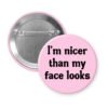 Pink pinback button with the text 'I'm nicer than my face looks' printed in black.