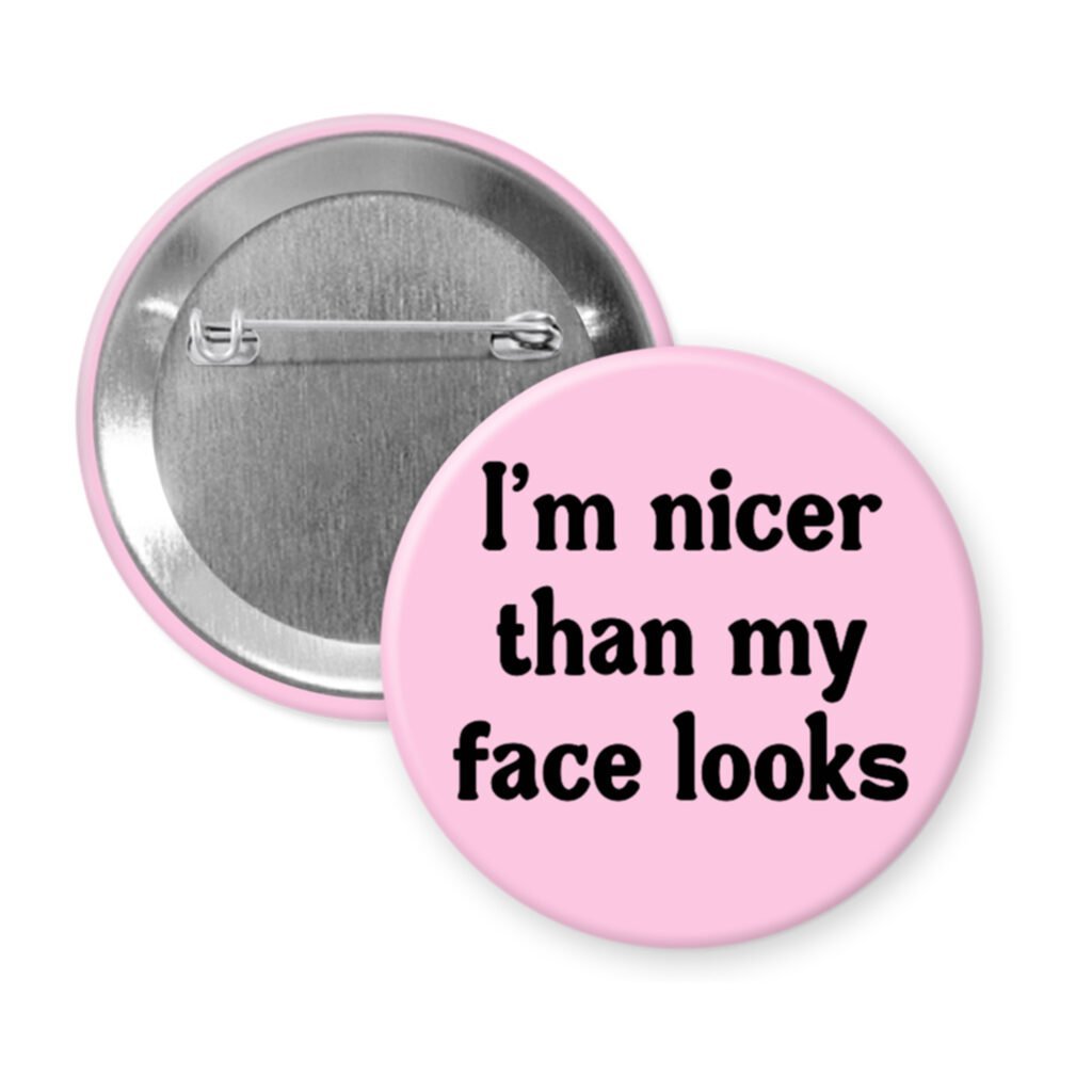 Pink pinback button with the text 'I'm nicer than my face looks' printed in black.
