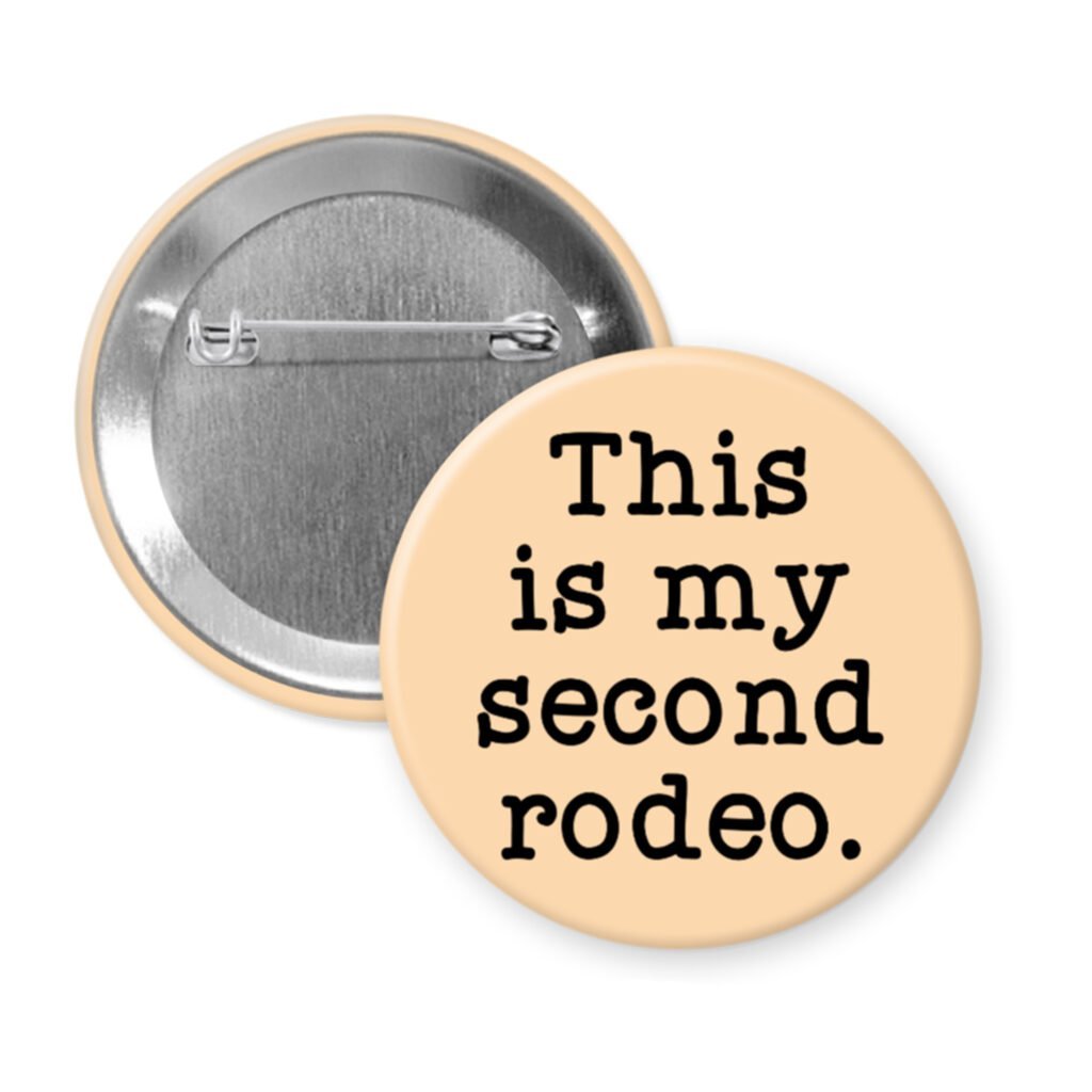 Peach color pinback button with the text 'This is my second rodeo.' printed in black.
