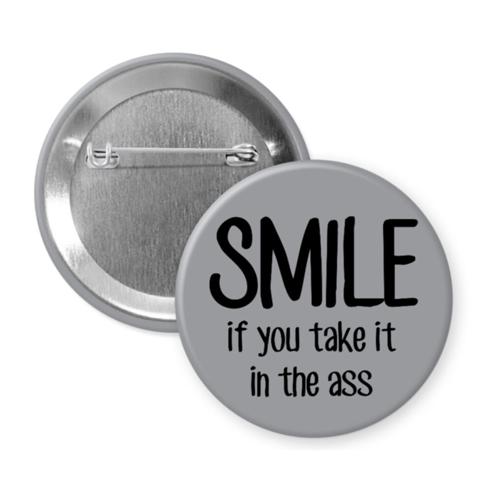 Grey pinback button with the text 'SMILE if you take it in the ass' printed in black.