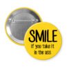 Yellow pinback button with the text 'SMILE if you take it in the ass' printed in black.