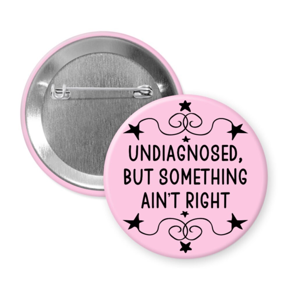 Pink pinback button with the text 'Undiagnosed, but something ain't right' printed in black.