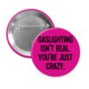 Pink button pin with the text 'Gaslighting isn't real. You're just crazy' in black distressed text.