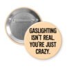 Peach button pin with the text 'Gaslighting isn't real. You're just crazy' in black distressed text.
