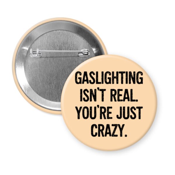 Peach button pin with the text 'Gaslighting isn't real. You're just crazy' in black distressed text.
