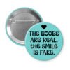 Blue pinback button with the text 'The boobs are real, the smile is fake'.
