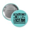 Blue pinback button with bold black text reading ‘Adulting is a Scam’ in mixed block and distressed fonts. The design includes a smiley face, star, and flower icons, with a checkerboard stripe along the bottom.