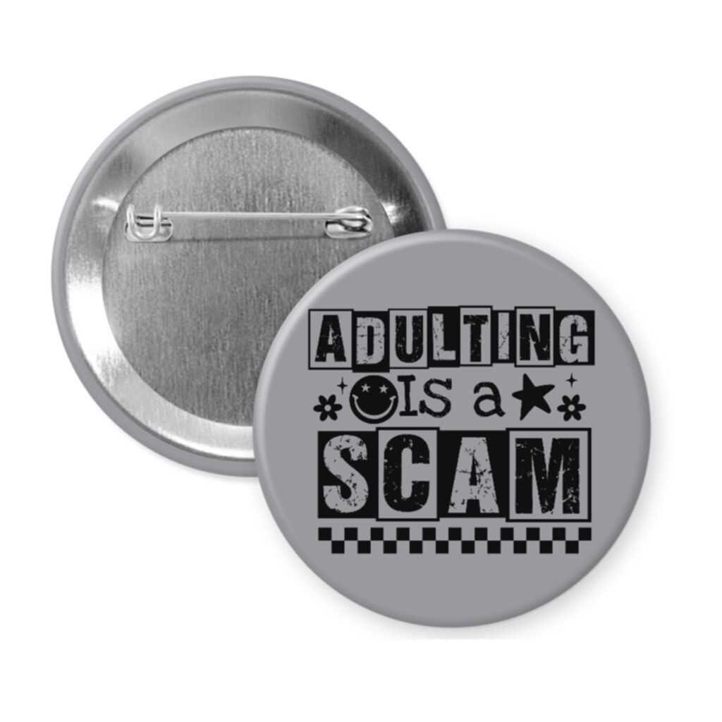 Grey pinback button with bold black text reading ‘Adulting is a Scam’ in mixed block and distressed fonts. The design includes a smiley face, star, and flower icons, with a checkerboard stripe along the bottom.
