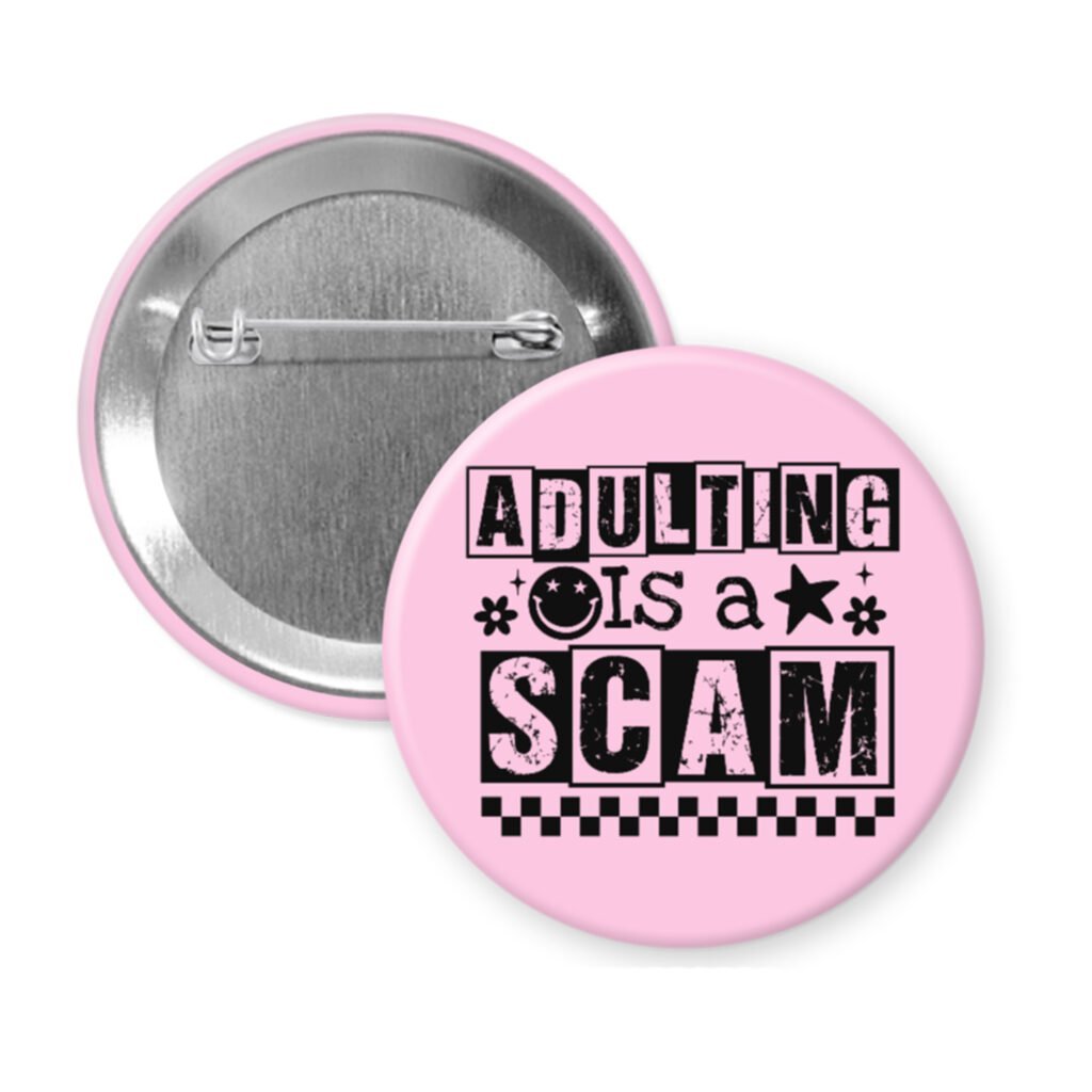 Pink pinback button with bold black text reading ‘Adulting is a Scam’ in mixed block and distressed fonts. The design includes a smiley face, star, and flower icons, with a checkerboard stripe along the bottom.