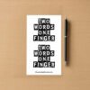 Sticker sheet with two bold black text designs reading TWO WORDS ONE FINGER, placed beside a pen on wood surface.