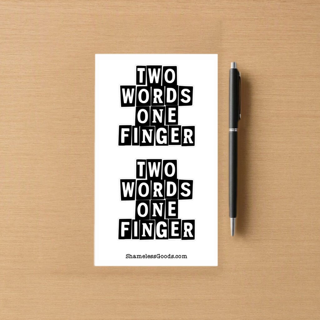 Sticker sheet with two bold black text designs reading TWO WORDS ONE FINGER, placed beside a pen on wood surface.
