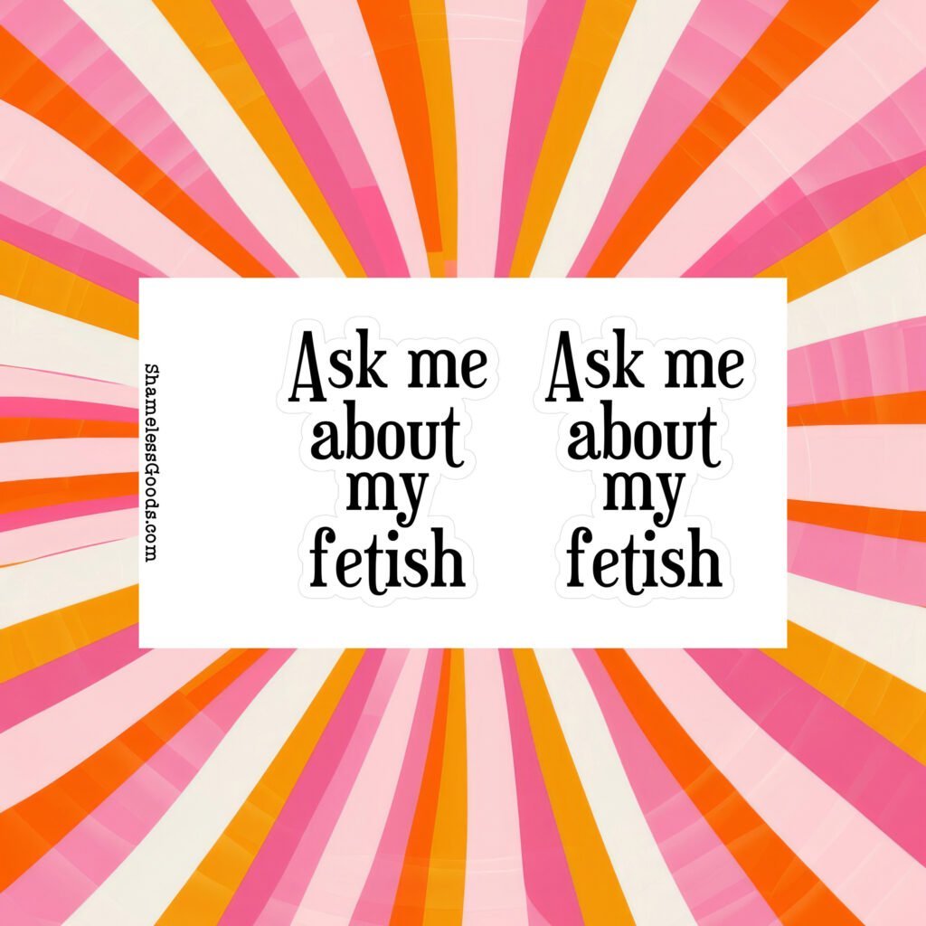 Sticker sheet on a wooden surface beside a black pen, featuring two identical black text designs that read Ask me about my fetish in bold serif font. Vertical branding text on the left reads ShamelessGoods.com.