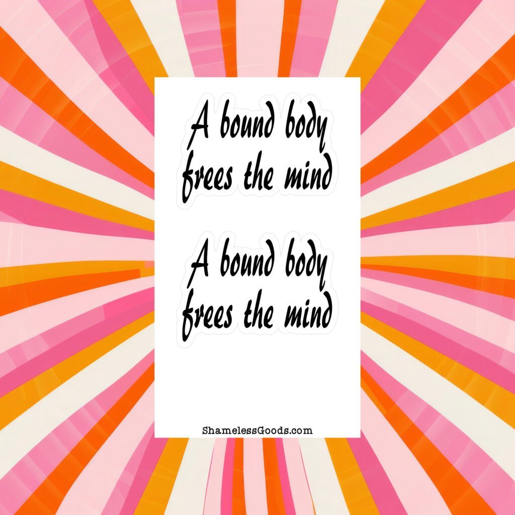 Sticker sheet on a wooden surface beside a black pen, featuring two identical black script phrases that read A bound body frees the mind, each outlined in white. Branding at bottom reads ShamelessGoods.com.