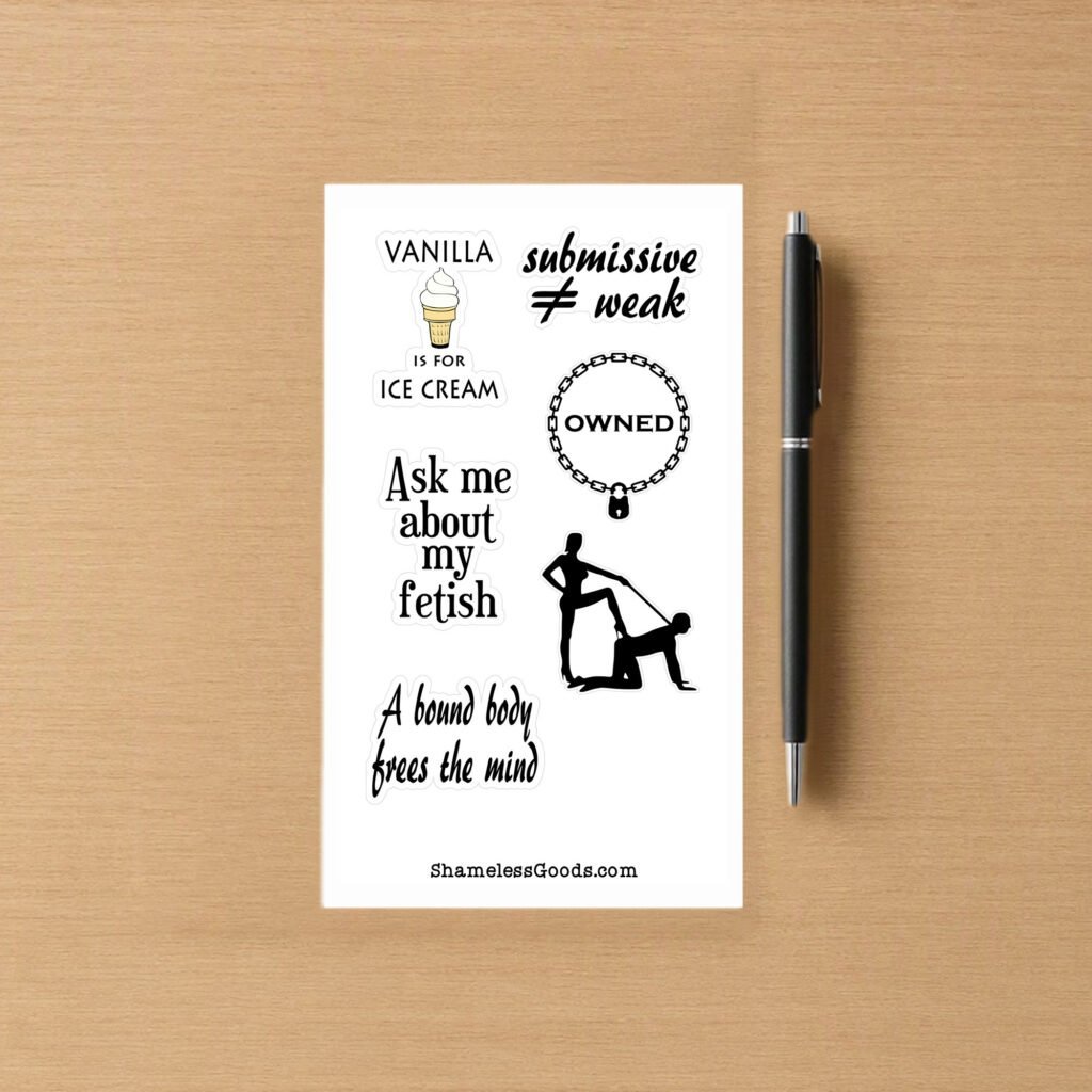 Sticker sheet on a wooden surface beside a black pen, featuring adult‑humor BDSM designs and phrases such as Vanilla is for ice cream, submissive ≠ weak, Ask me about my fetish, and a silhouette of a dominant‑submissive pose. Branding at bottom reads ShamelessGoods.com.