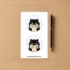 Sticker sheet with two round designs showing a black cat holding an open book that reads Is He Dead Yet in bold letters.